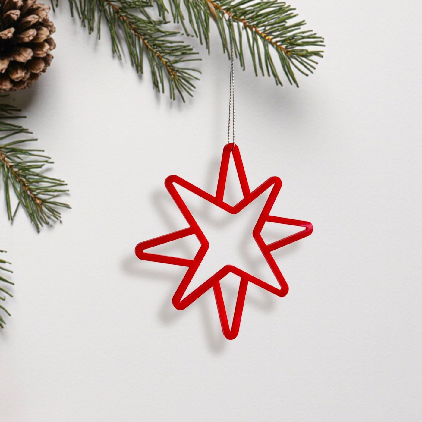 A red star-shaped ornament is hanging from a branch of a pine tree, with pine needles visible on the left side of the image.