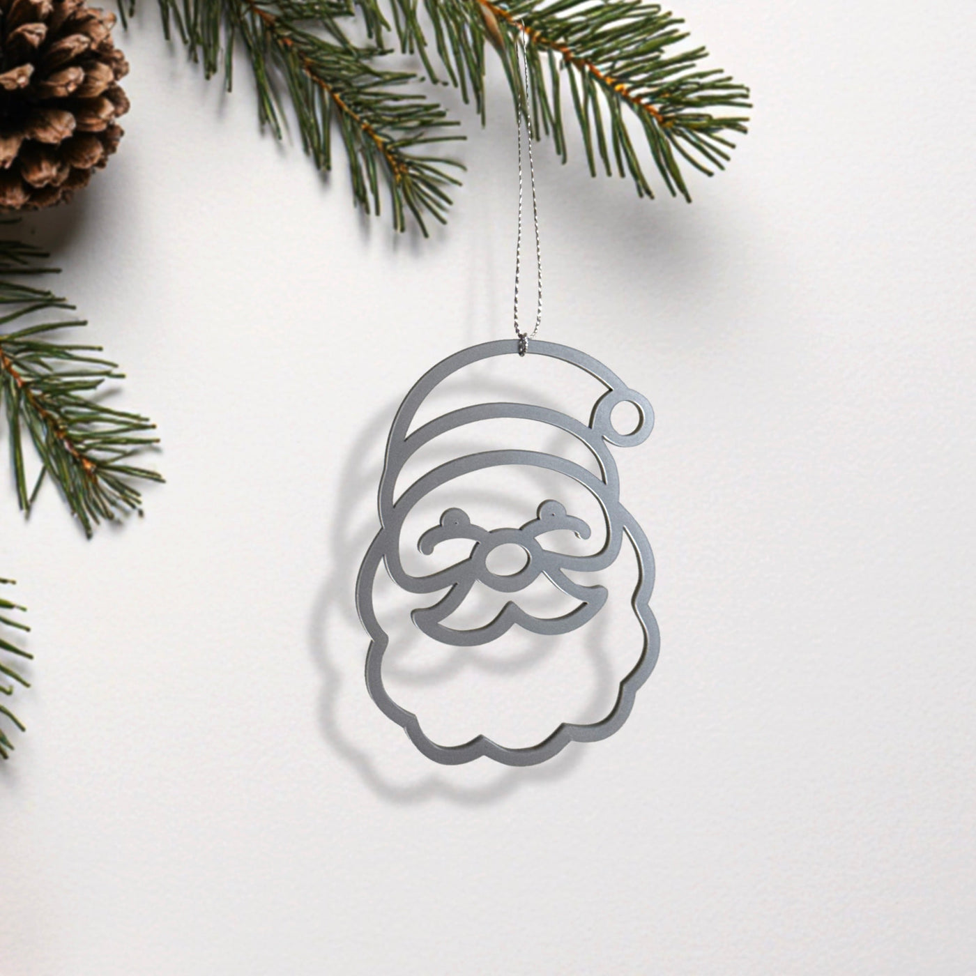 A silver ornament resembling a smiling face is hanging from a branch of a pine tree.