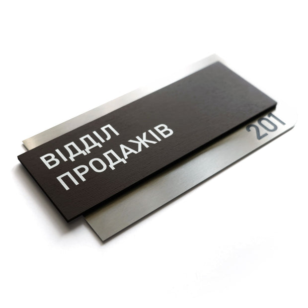 a black rectangular sign with white text, which appears to be a nameplate or sign with a name and possibly a number.