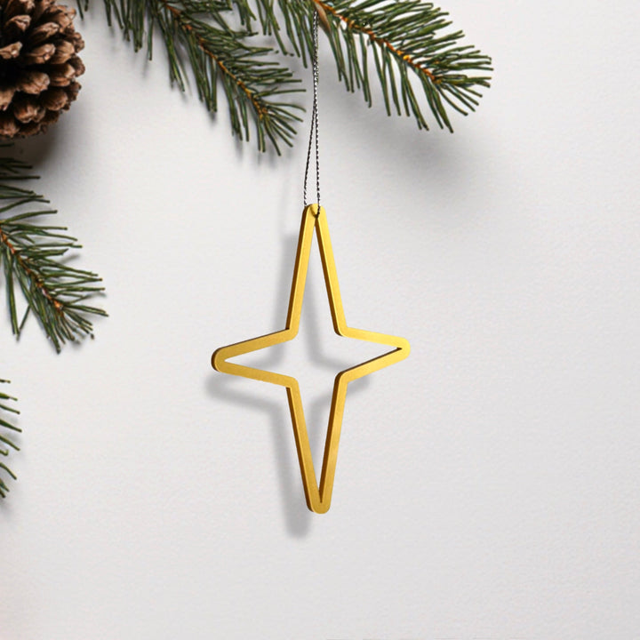 A golden star-shaped ornament is hanging from a branch of a pine tree, with pine needles and a pine cone visible in the background.