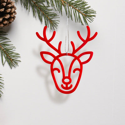 A red deer head ornament with antlers is hanging from a string, surrounded by pine branches and pine cones.