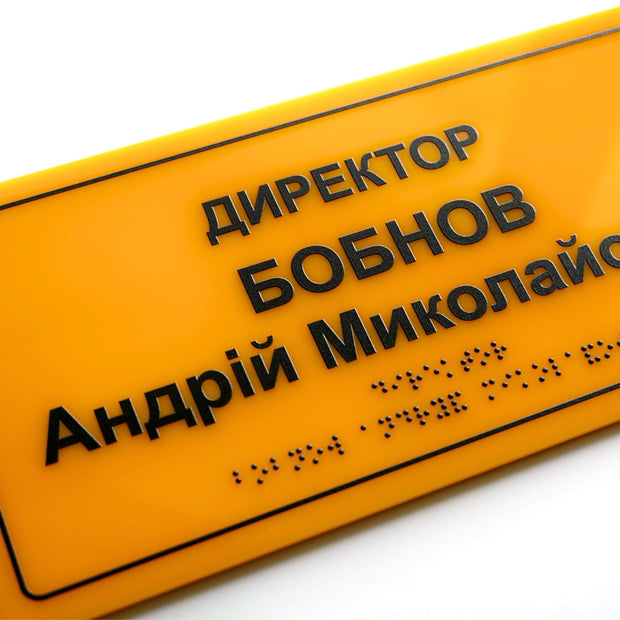 Крупний план іменної таблички «Директор» зі шрифтом Брайля, жовтий акрил і рельєфний чорний текст