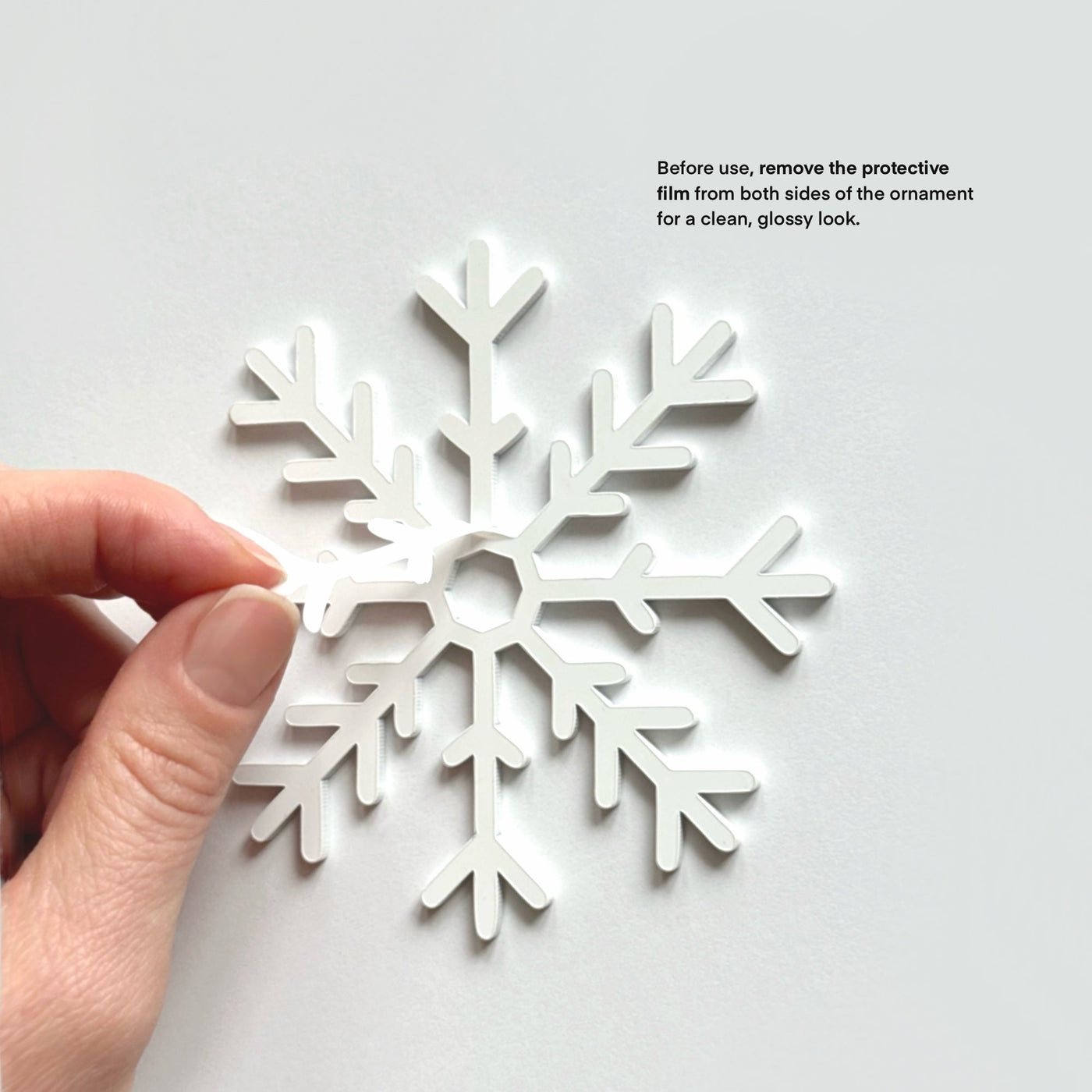 A hand is holding a white snowflake ornament against a white background.