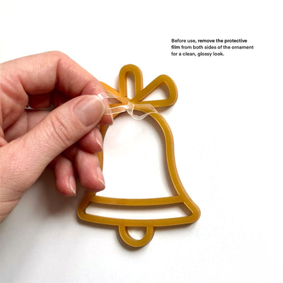 A hand is holding a yellow bell-shaped ornament with a clear plastic film on both sides, as indicated in the instructions.