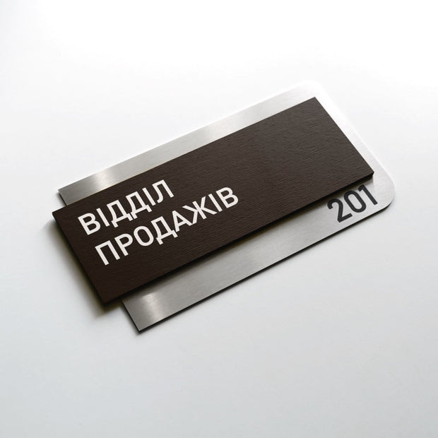 a dark brown rectangular sign with white text, placed on a white surface.